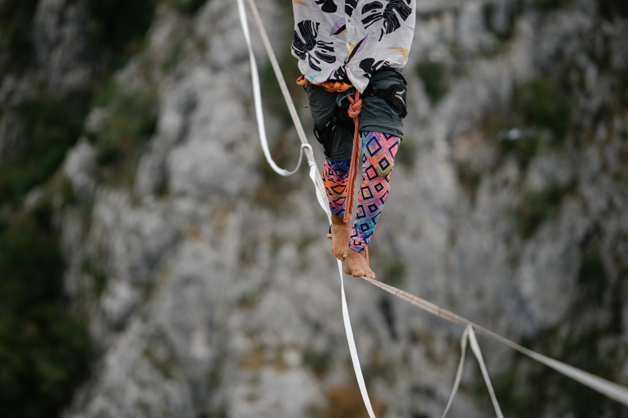 person in harness and colorful leggings walking barefoot on highline above rocky terrain