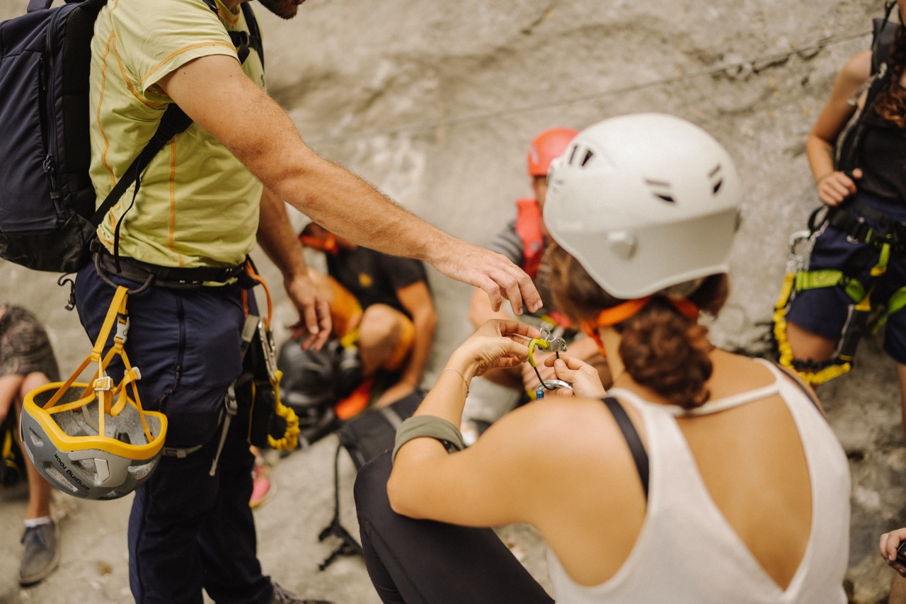 group of people with climbing gear preparing and assisting each other near a rocky surface