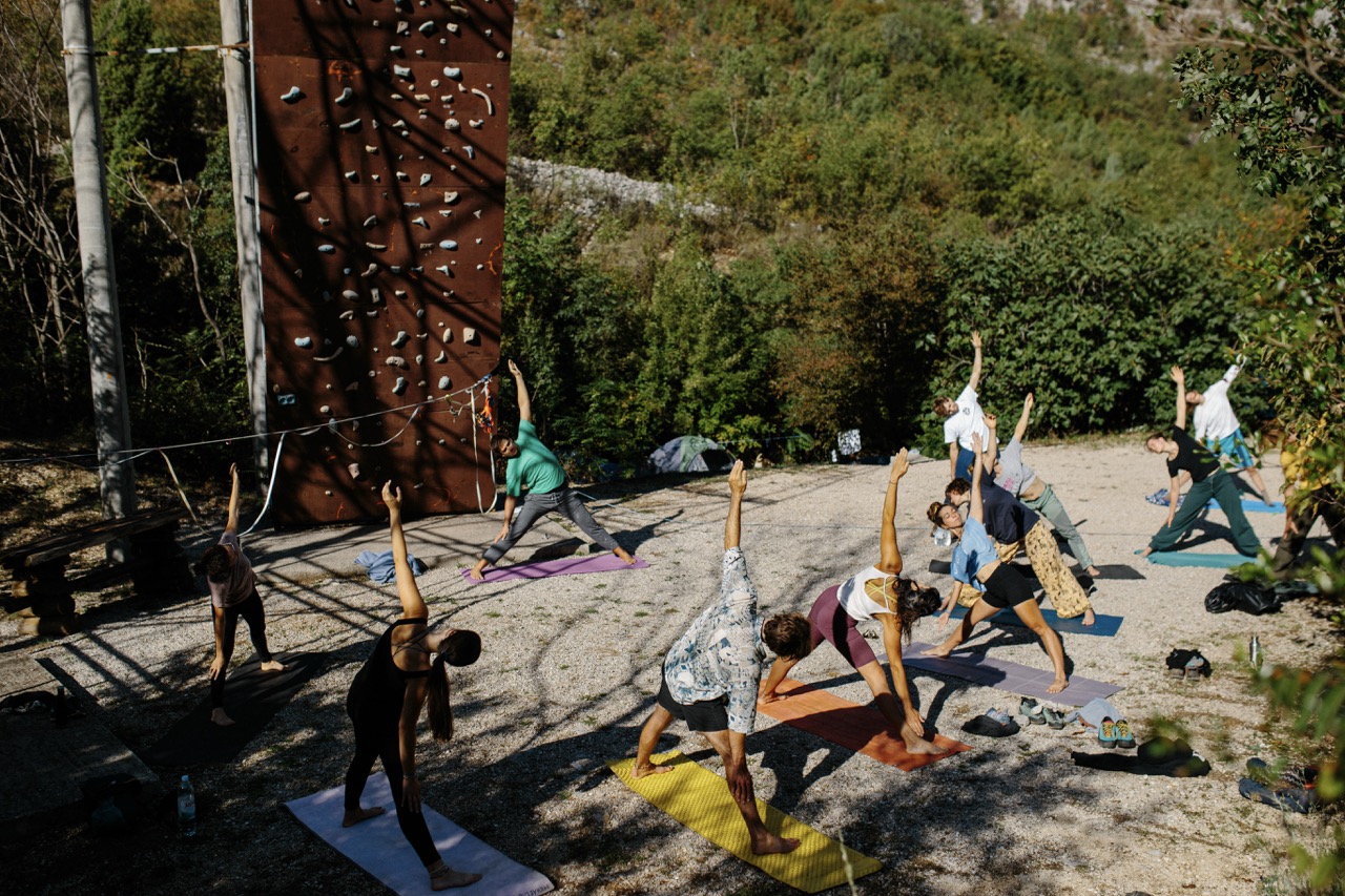 group of people practicing yoga outdoors near a climbing wall on mats
